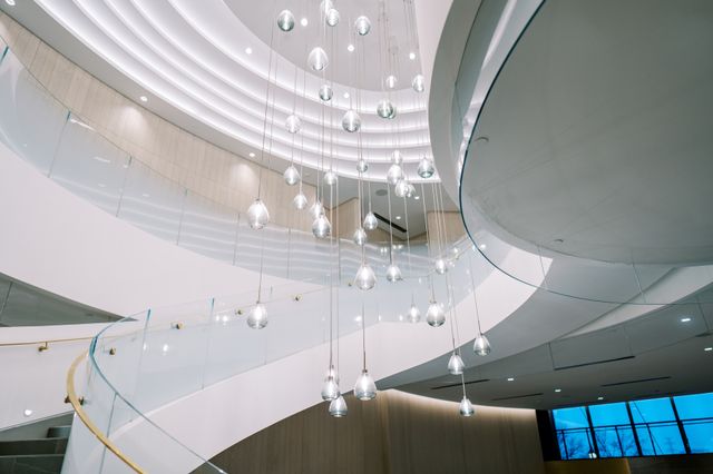 A sweeping staircase with glass balustrades curves around a cluster of suspended glass lights.