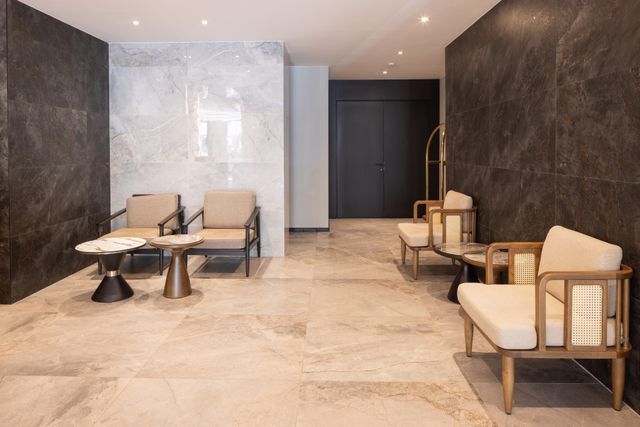 Pale lounge chairs and small tables sit between dark stone walls in a compact lobby seating area.