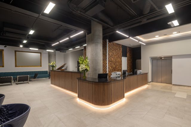 A curved timber reception desk with concealed lighting sits beneath a dark ceiling in an open lobby.