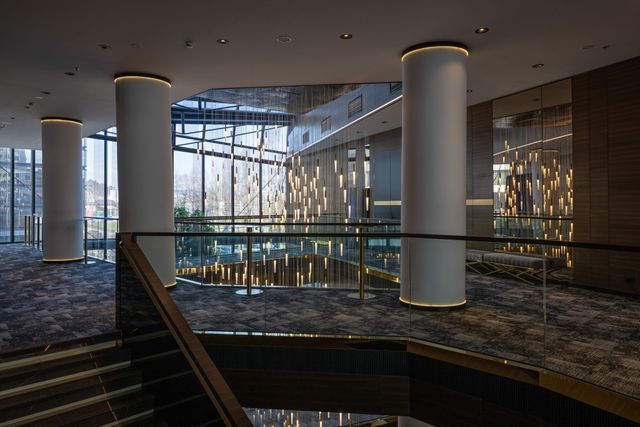 Tall columns, an open stairwell and suspended lighting define a large lobby with expansive windows.
