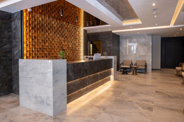 A stone reception counter and a sculptural timber screen introduce a lobby with warm lighting and lounge seating.