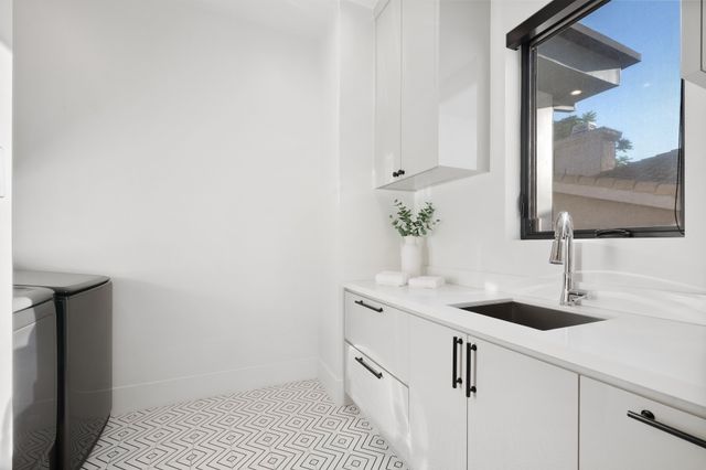 White cabinetry and a deep sink sit beneath a dark-framed window above a geometric patterned floor.