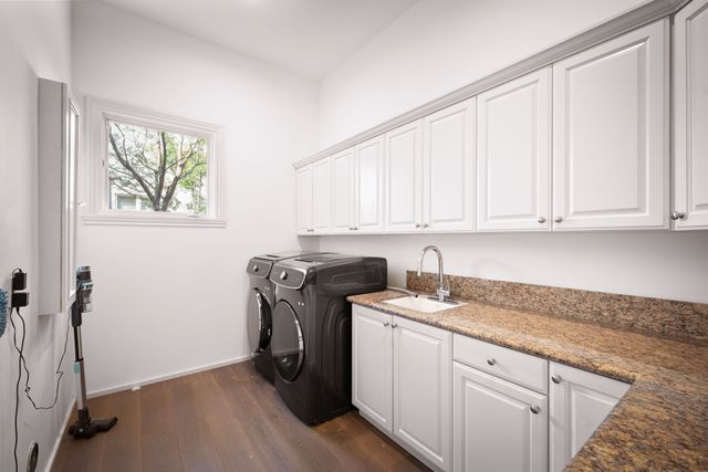 Dark laundry appliances sit beside long white cabinets, a sink and a mottled stone countertop.