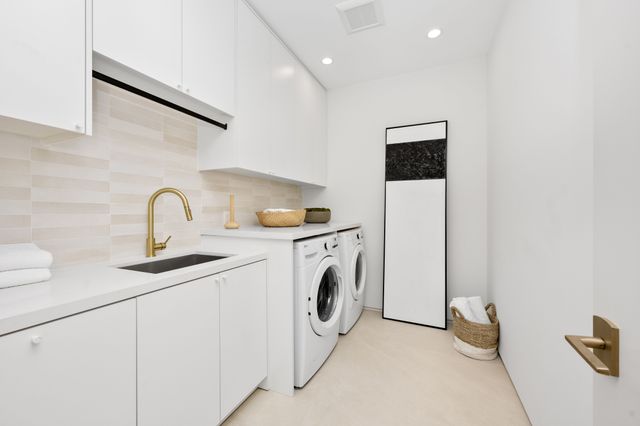 White cabinetry and front-loading appliances share a compact laundry room with a gold-toned tap and pale floor.