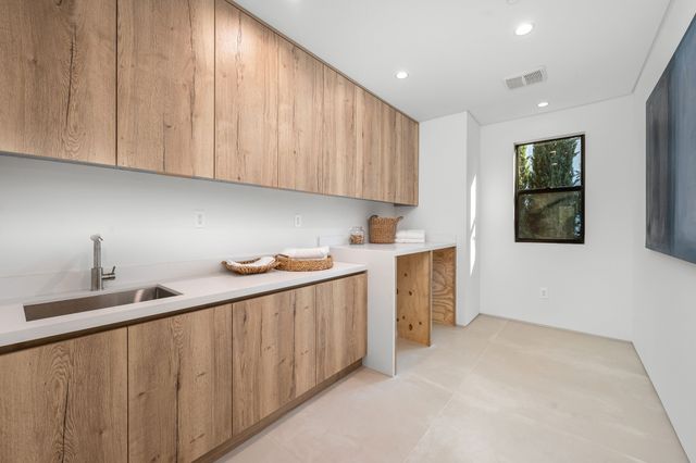 Long timber cupboards and a pale worktop surround a sink in a bright fitted utility room.