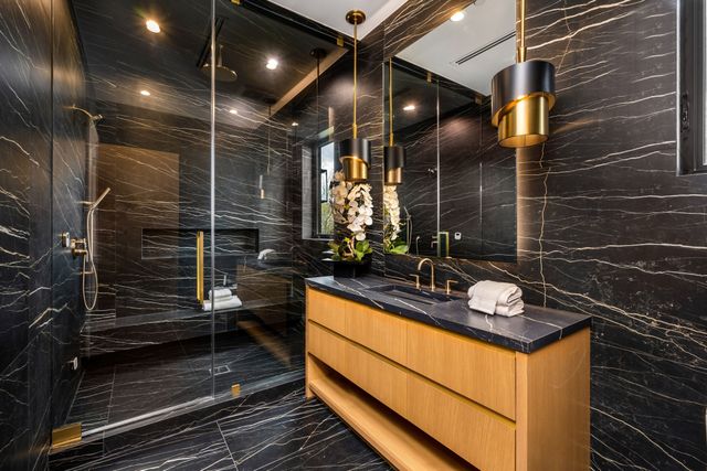Dark veined stone surrounds a glass shower and timber vanity with gold-toned pendant lights and fixtures.
