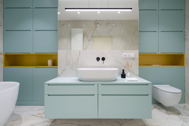 Muted blue cabinetry and gold-toned niches frame a white basin beneath a wide bathroom mirror.