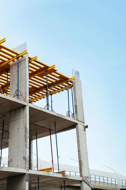 Concrete columns and floor slabs support yellow formwork beams and slender temporary props beneath an open sky.