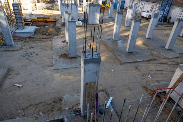 Rows of concrete columns and exposed reinforcement rise from individual footings across an active construction site.