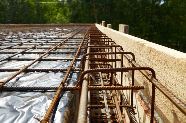 Steel mesh and a rectangular reinforcement cage run alongside timber edge formwork above a reflective membrane.