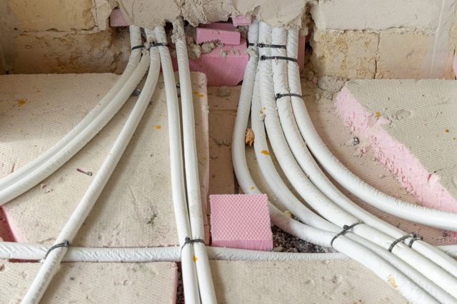 White wrapped service lines cross exposed floor insulation and enter an unfinished wall, with bundles secured by dark ties.