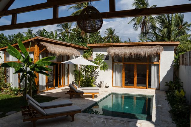 Timber-framed resort rooms with shaded openings surround a small pool, lounge chairs and tropical planting.