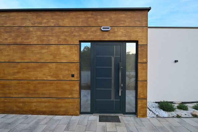 A dark entrance door and narrow glazed sidelights sit within warm-toned horizontal wall panels beside a white exterior wall.