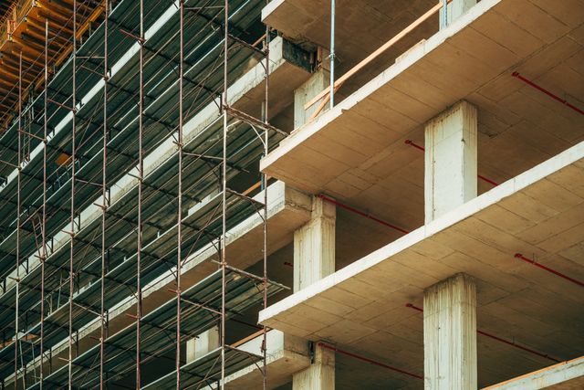 Concrete floor slabs and columns form an unfinished multi-storey building, with metal scaffolding rising along one side.