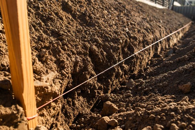 A taut string is tied around a timber stake and extends along a freshly excavated trench in warm sunlight.