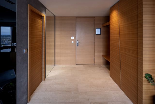 A hotel suite entrance has timber wall panels and cupboards, a tall mirror, integrated shelving and a pale stone floor.