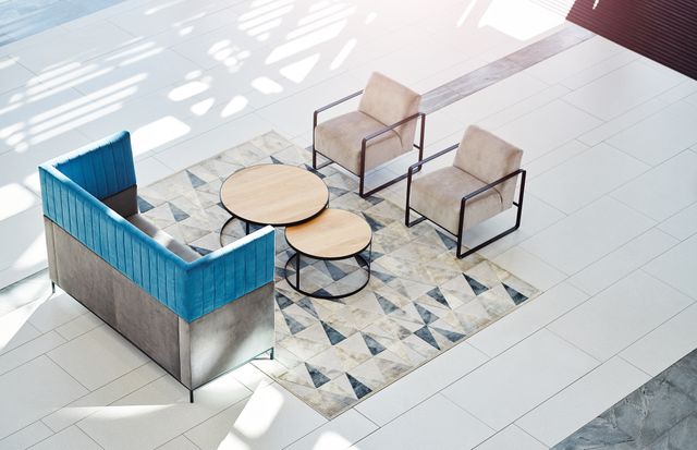 A high-backed blue and grey sofa faces two pale armchairs across round nesting tables on a patterned rug.