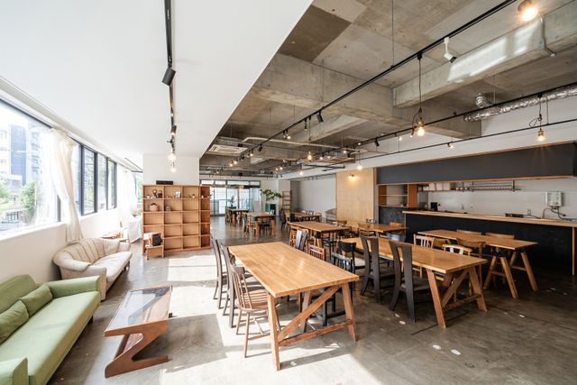 Wood-tone tables and mixed chairs fill a bright cafe-style room, with sofas by the windows and a long service counter.