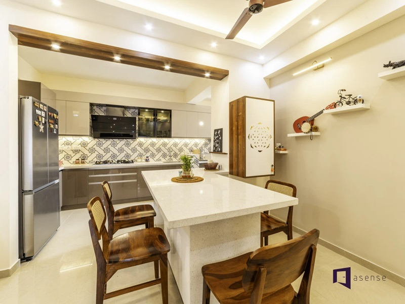 This shows an open-concept modular kitchen and dining area featuring glossy beige cabinetry, a patterned tile backsplash, and a large white stone breakfast island paired with wooden chairs.