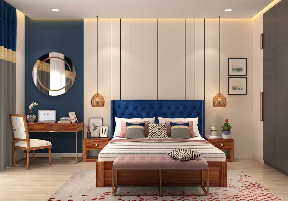 This image illustrates a modern bedroom with a tufted blue headboard, a vertically paneled accent wall flanked by hanging pendant lights, and an adjacent wooden study desk set against a blue backdrop.